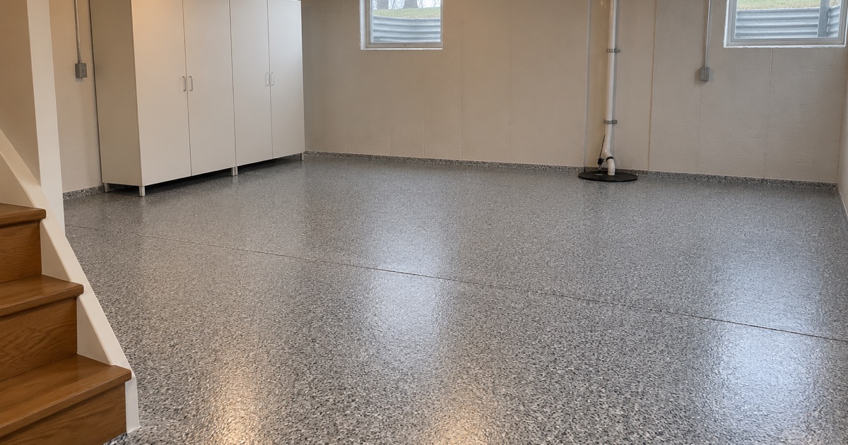 An empty, finished flake basement floor in a Tinley Park two-story, running clean to the sump rim and the foot of the stair.